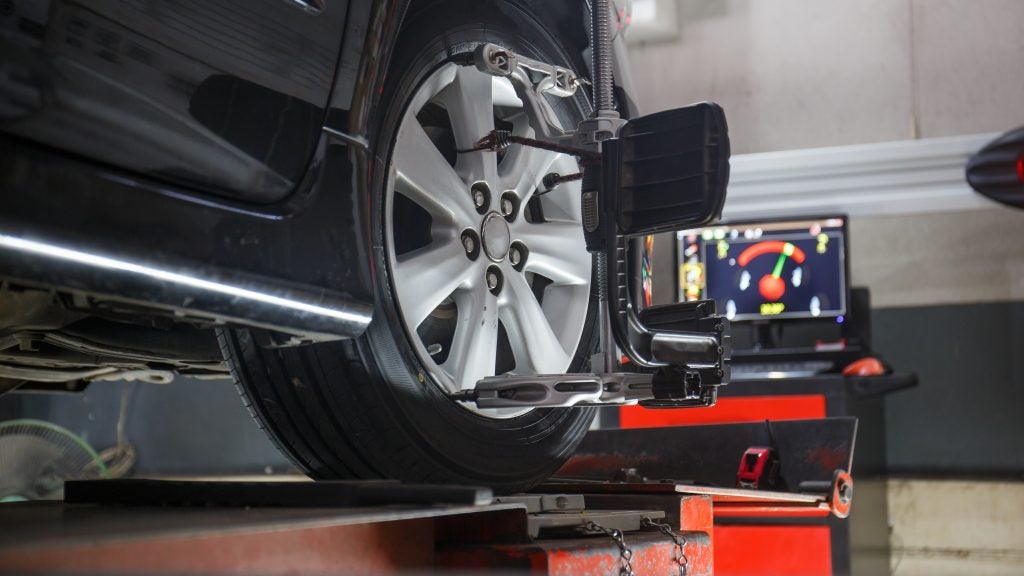 Black car undergoing a wheel alignment check, with sensors attached to the tires and a monitor in the background.