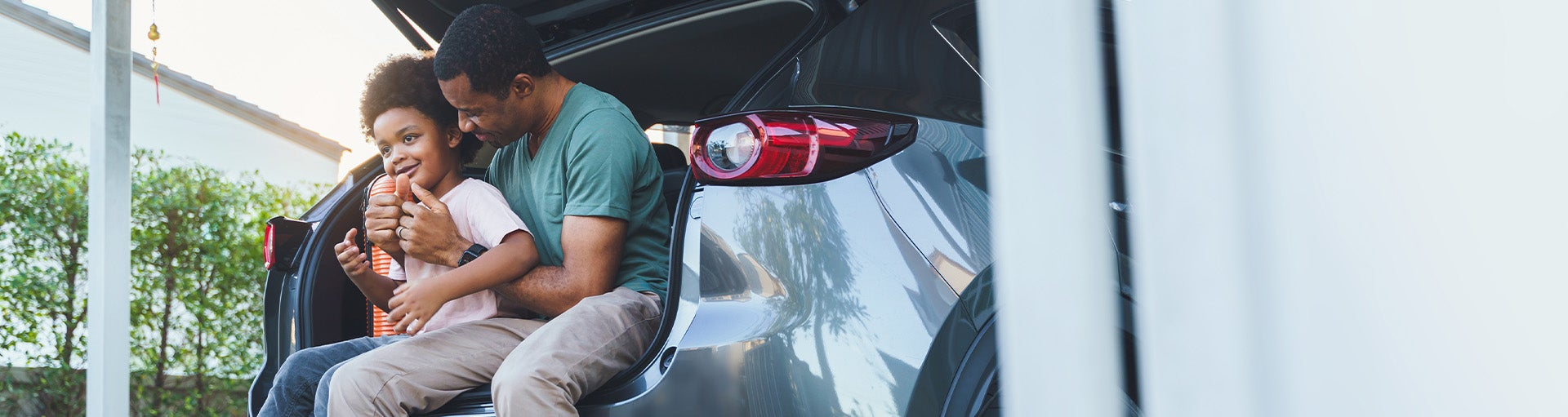 A father sitting in the cargo space of his SUV with his child on his lap.