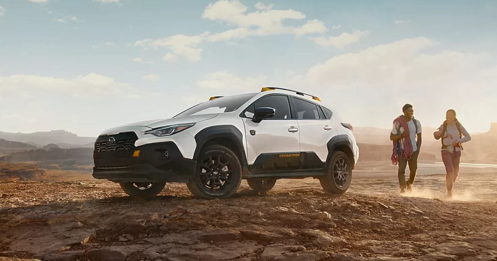 A couple carrying rock climbing gear walking towards a white 2024 Subaru Crosstrek Wilderness
