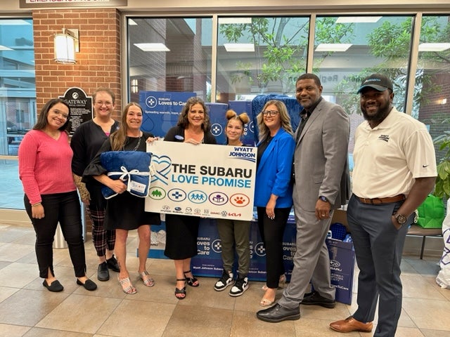 A group photo showcasing Wyatt Johnson Subaru's Love Promise donation boxes and their partners.
