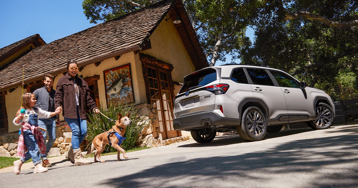 A family walking their dog past their Subaru Forester parked in the driveway.