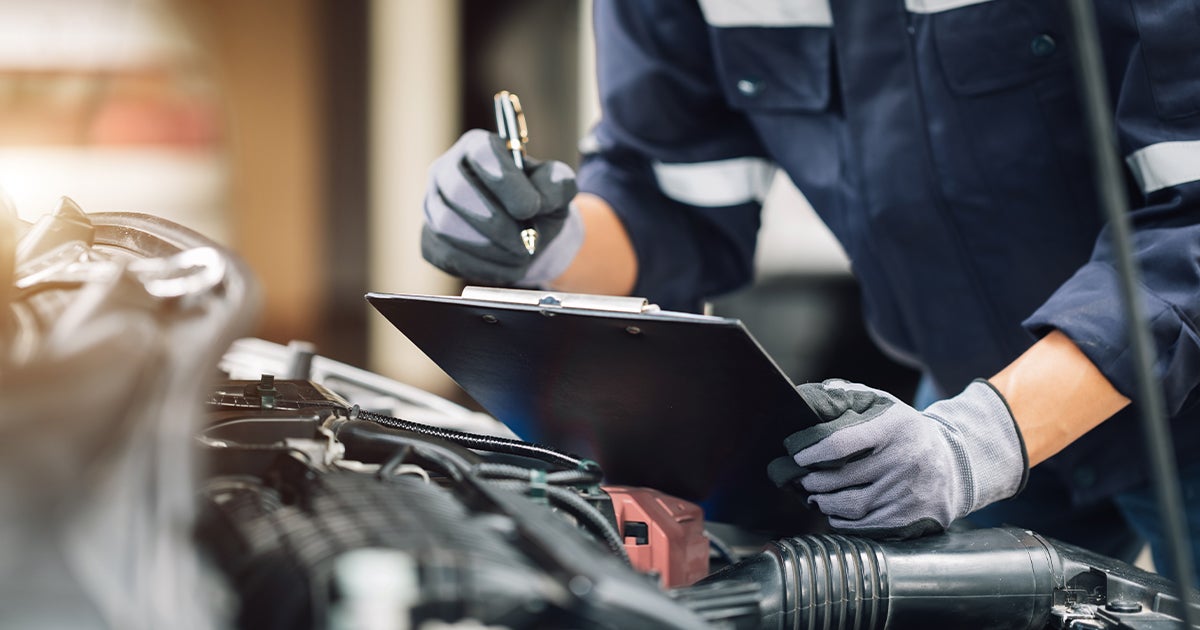 A close-up of a service technician holding a clipboard surveying a vehicle's engine in the service center