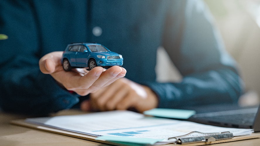A person holding a blue car while signing auto financing paperwork.