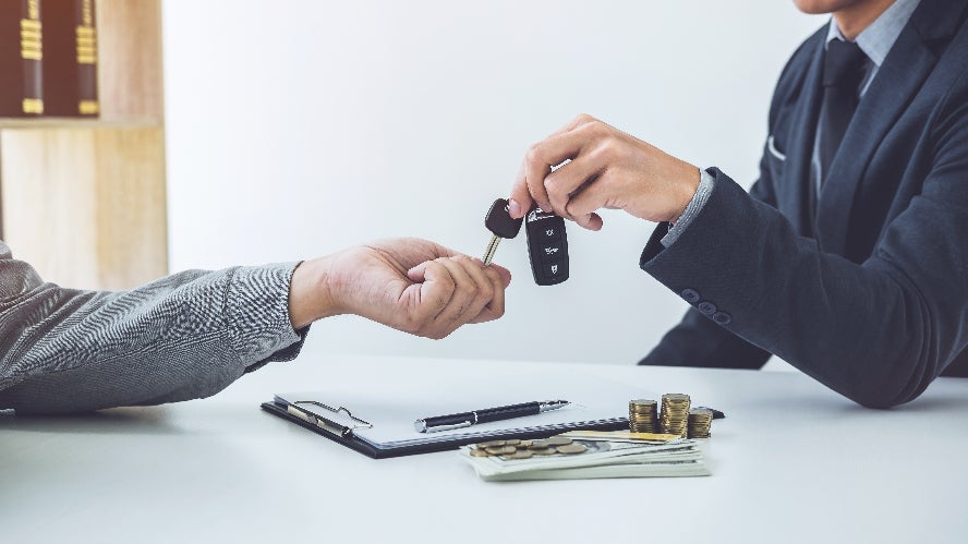 A salesperson passing over car keys to someone after signing a financial contract.