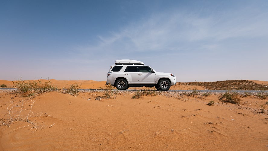 A white SUV driving on the road in a desert.