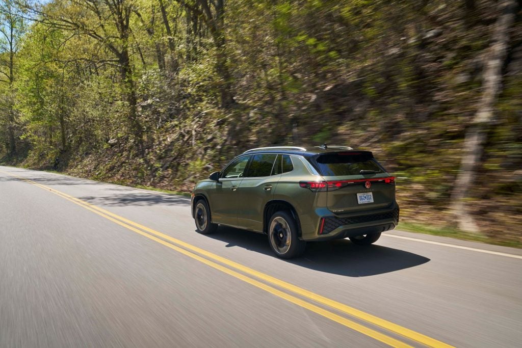 The Dark Green Back Exterior Of The 2026 Volkswagen Tiguan, Passing High Hills With Greenery And Trees