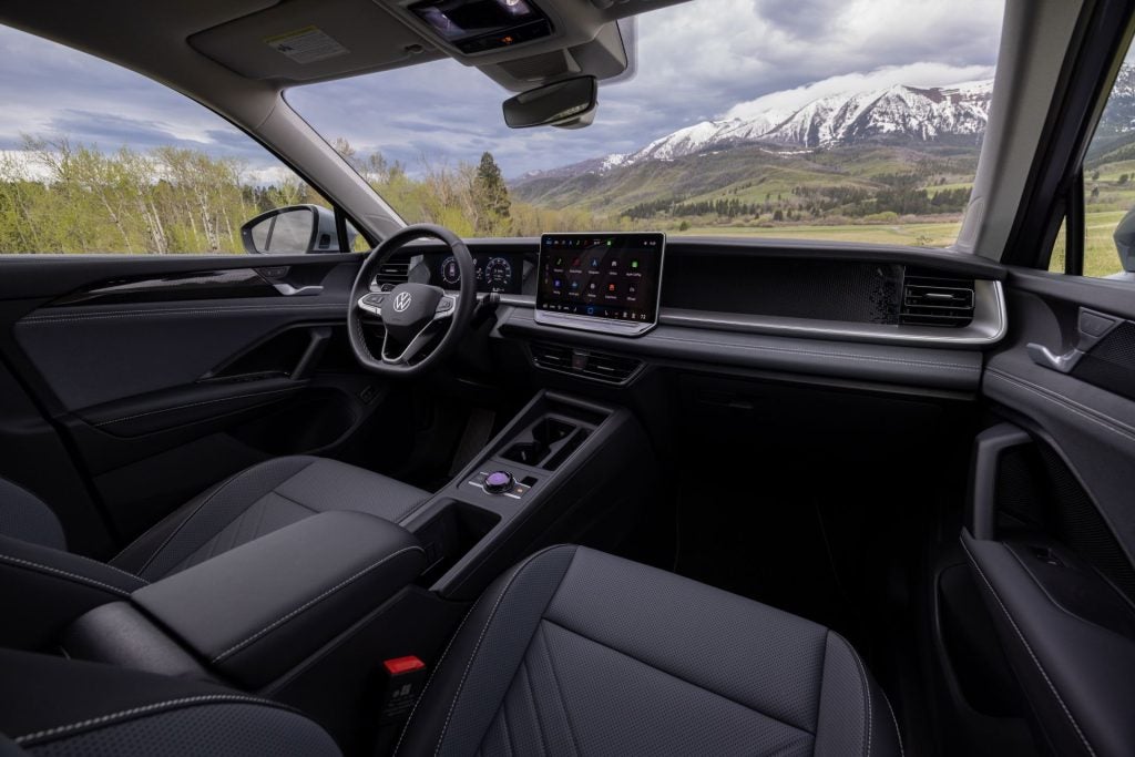The Sleek Black Interior Of The Wonderful Volkswagen Tiguan, With Snowy Magnificent Mountains and Sparse Trees Seen Through The Car's Front Windows