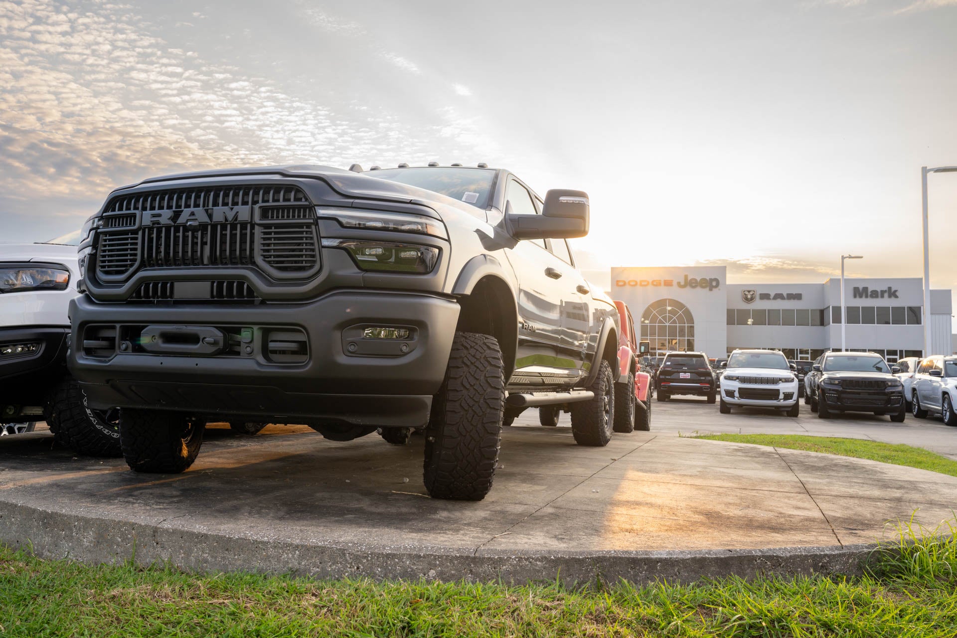 Close-up front three-quarter view of a dark Ram 2500 on a display pedestal at sunset, with the Mark Dodge dealership building lit behind it.