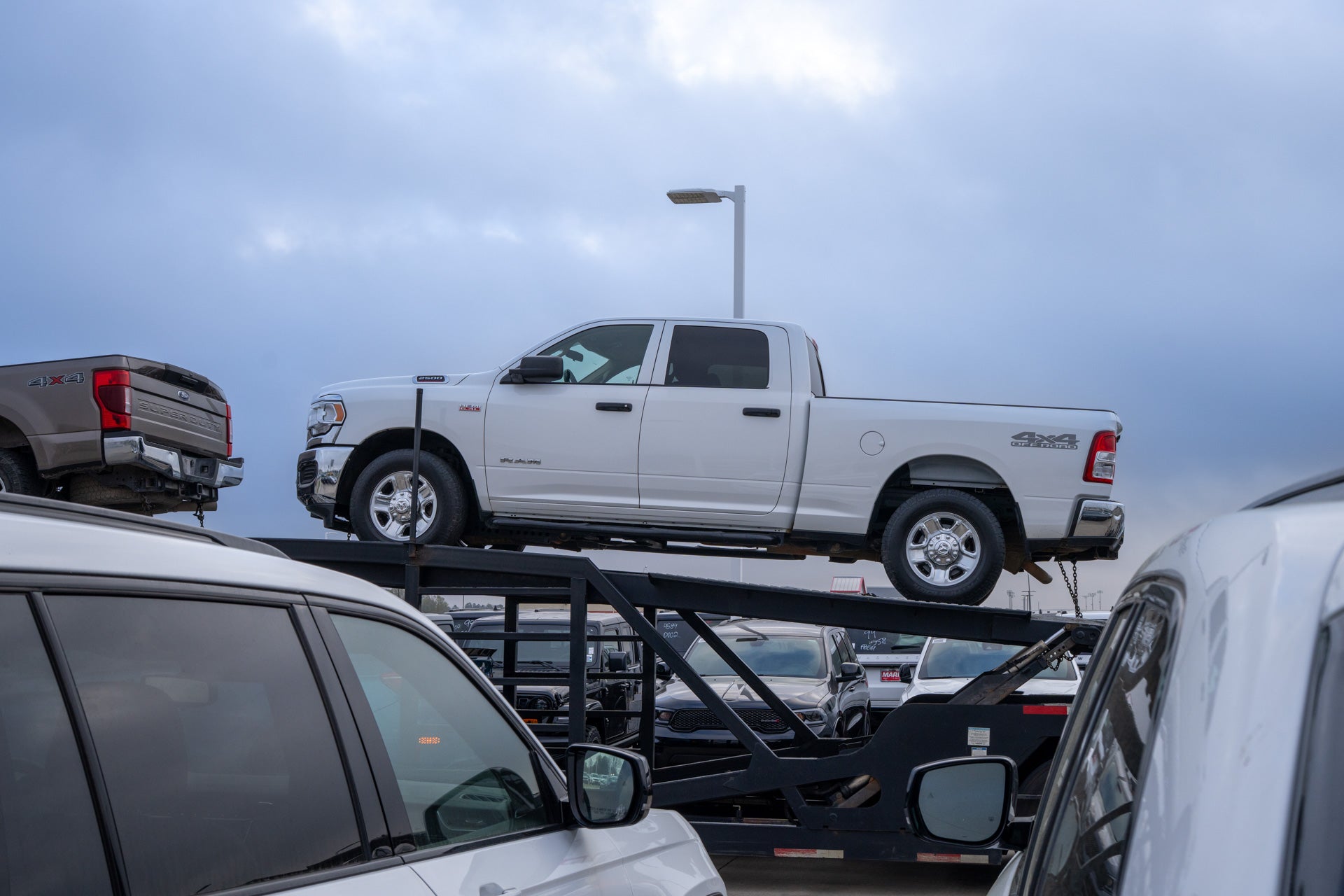 A white Ram 2500 pickup being unloaded from the top rack of a car-carrier delivery trailer at Mark Dodge.