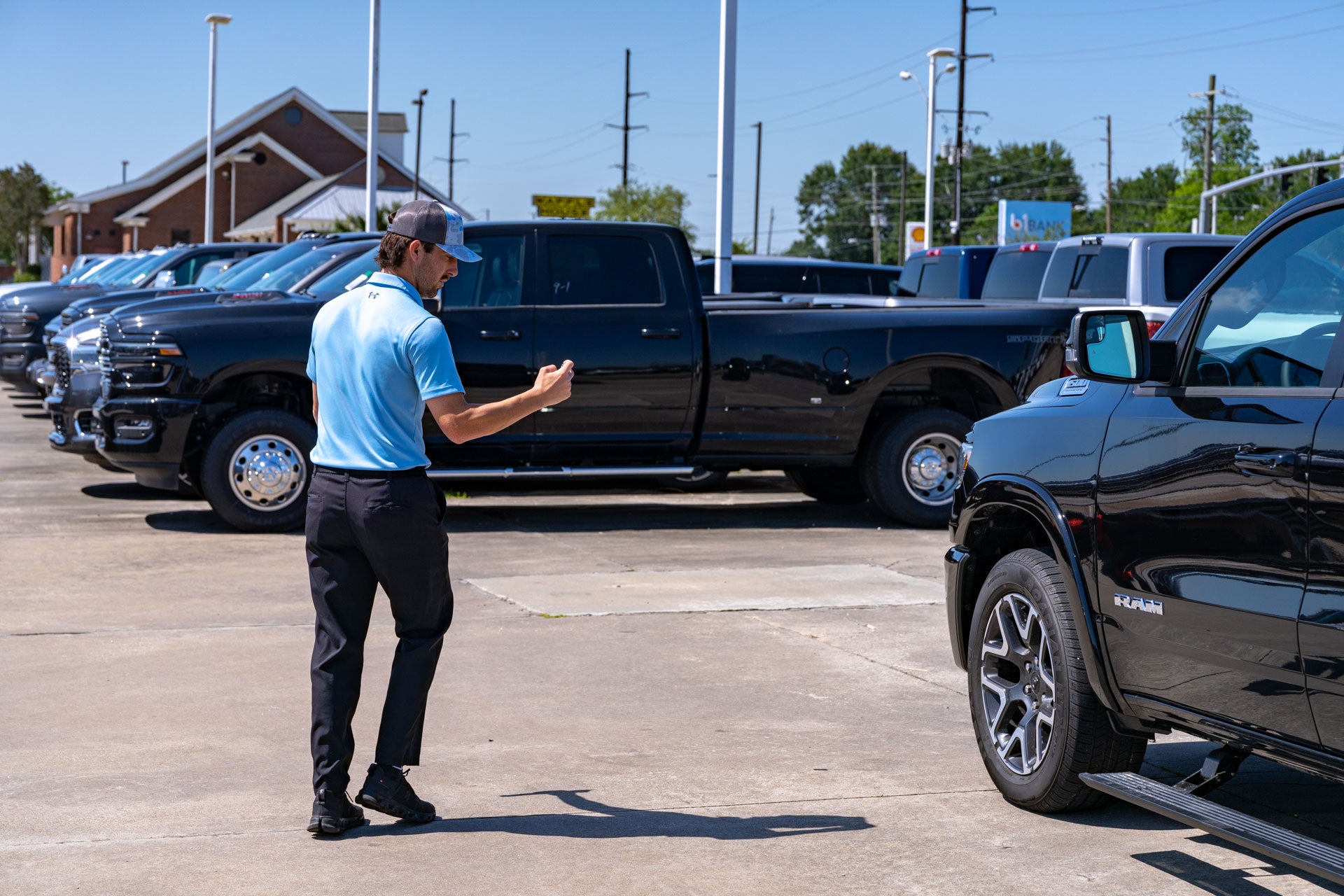 A Mark Dodge staff member in a light blue polo photographs a black Ram pickup with his phone in the lot, with other Ram trucks lined up nearby.