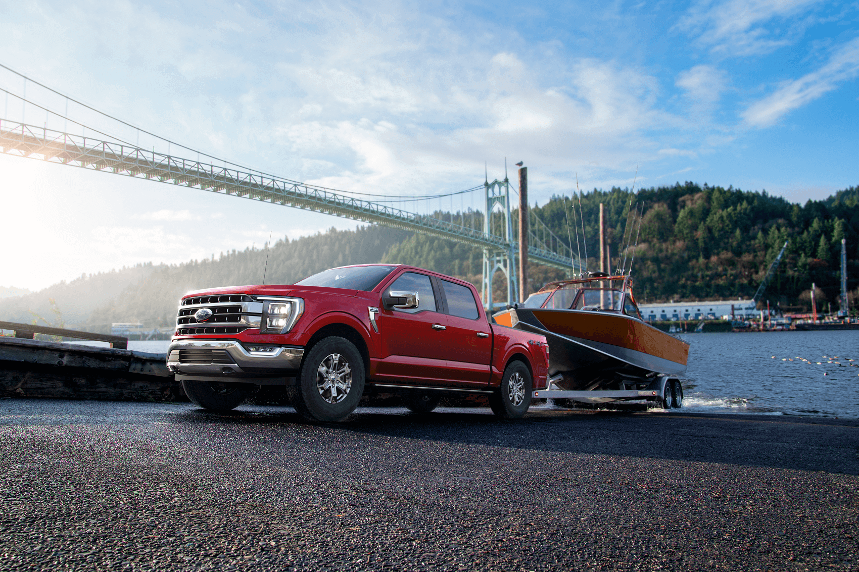 A new red 2021 Ford F-150 hauling a boat out of the water with a bridge in the background.