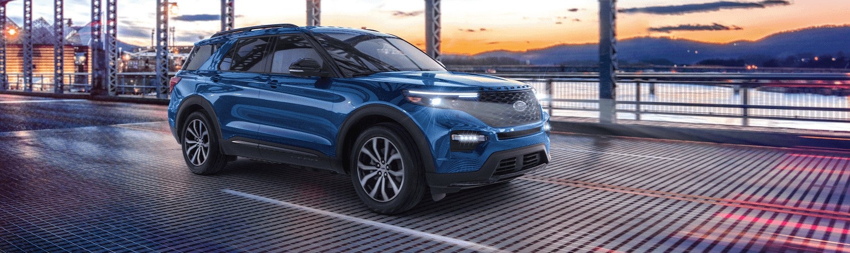 A new blue 2021 Ford Explorer driving during sunset over a bridge.