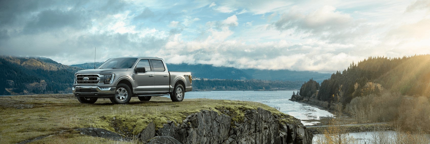 A new green 2021 Ford F-150 on a cliff with a lake and trees and hills in the distance.