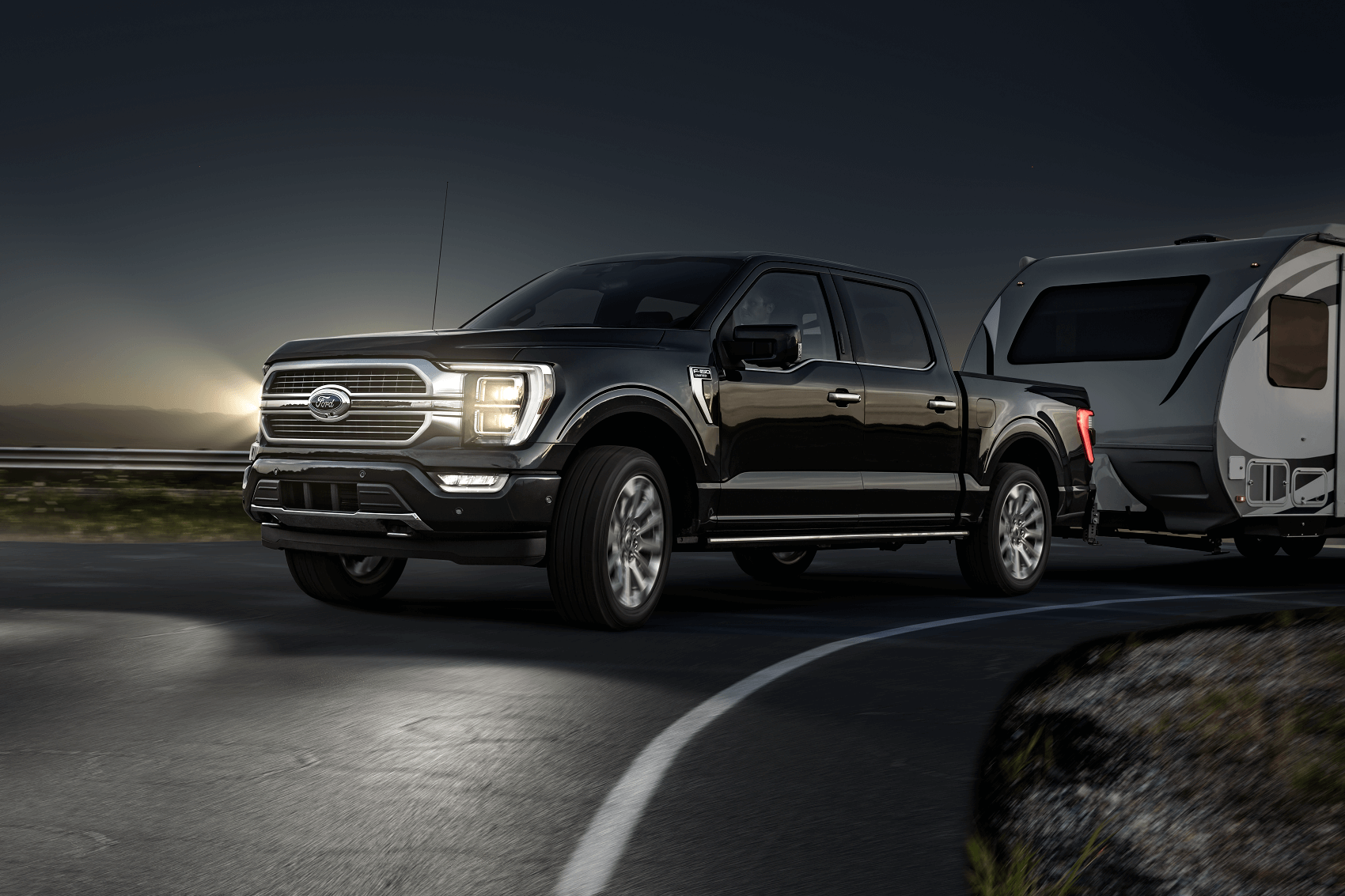 A new black 2021 Ford F-150 with it's headlights on towing a trailer in the dark.