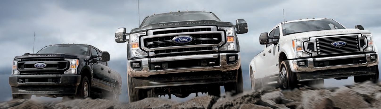 Three new 2021 Ford Super Duty F-250 trucks on the top of a cliff with black, grey and white exteriors from right to left. 