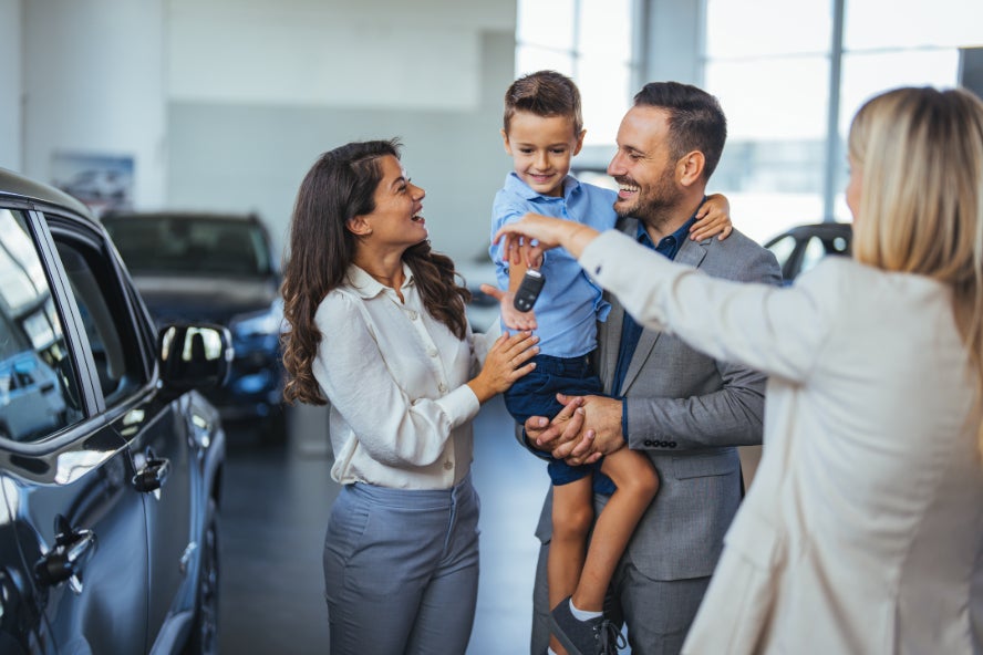 A family of three receiving keys to their new car from a salesperson.
