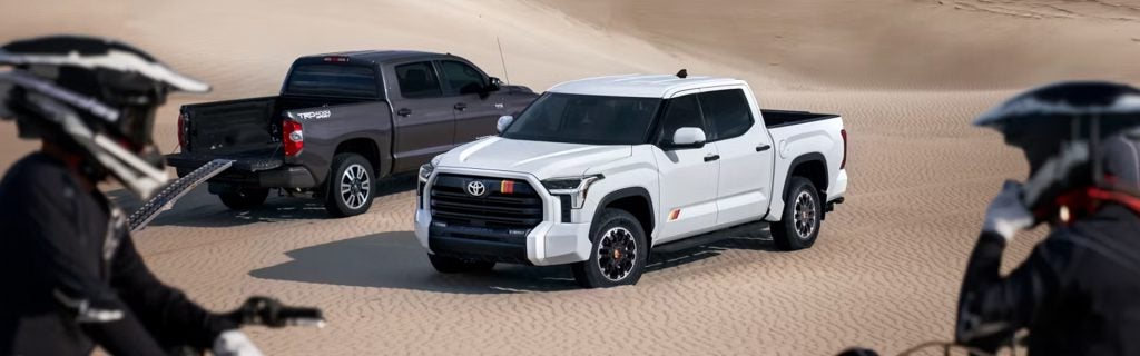 Two Toyota Tundra trucks, a white and a grey, parked on sand dunes