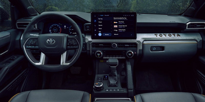 Interior view of a Toyota truck, showcasing the dashboard, steering wheel, large infotainment screen, and gear shift.