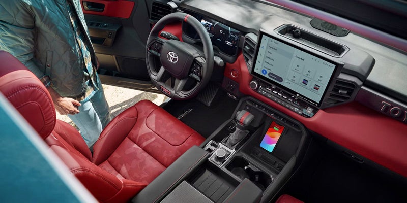 Interior of a modern truck with red seats and trim, a large touchscreen, and a phone wirelessly charging.