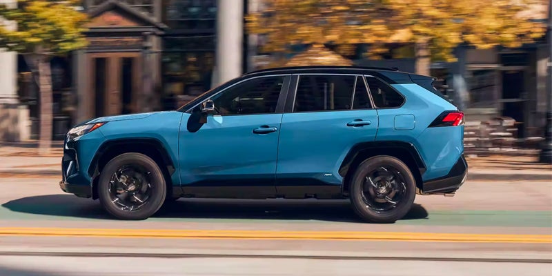 A blue SUV with a black roof and black trim drives down a city street, motion blur visible.