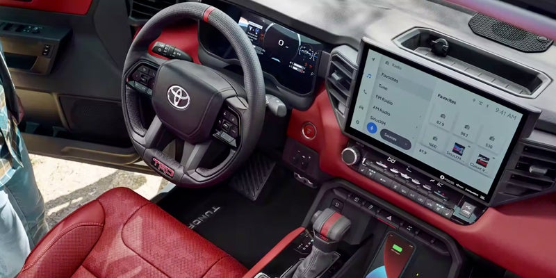Interior view of a modern car, featuring a black steering wheel with red accents and a large infotainment screen.