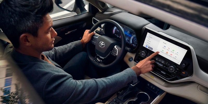 Man in a car, hands on the steering wheel, using the touchscreen infotainment system.