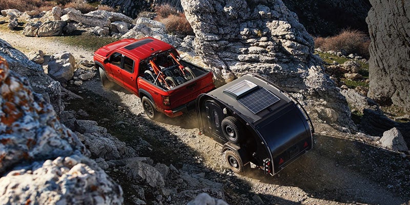 Red pickup truck with bicycles in its bed towing a black teardrop camper with solar panels up a rocky mountain road.