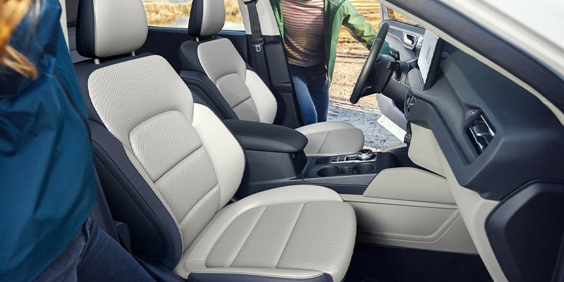 Interior of a car with white and dark blue leather seats, showing a person getting into the driver's side.
