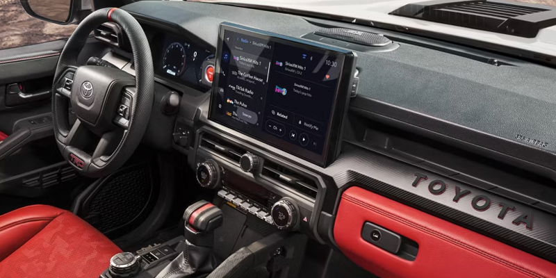 Interior of a car with black and red accents, including a large infotainment screen, steering wheel, and red seats.
