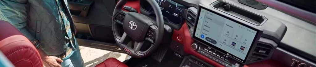 View inside a Toyota truck with dark red leather seats, displaying a large infotainment screen and a steering wheel.