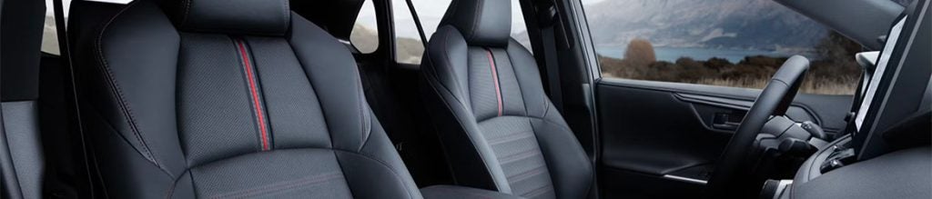 Interior view of a car with two black seats featuring red stripes, overlooking a lake and mountains.