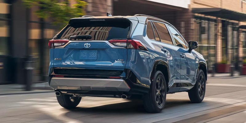 Rear view of a blue 2024 Toyota RAV4 Hybrid XSE driving down a city street.