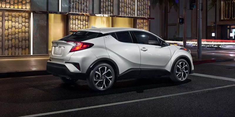 White Toyota C-HR parked at night on a city street, seen from the rear passenger side.