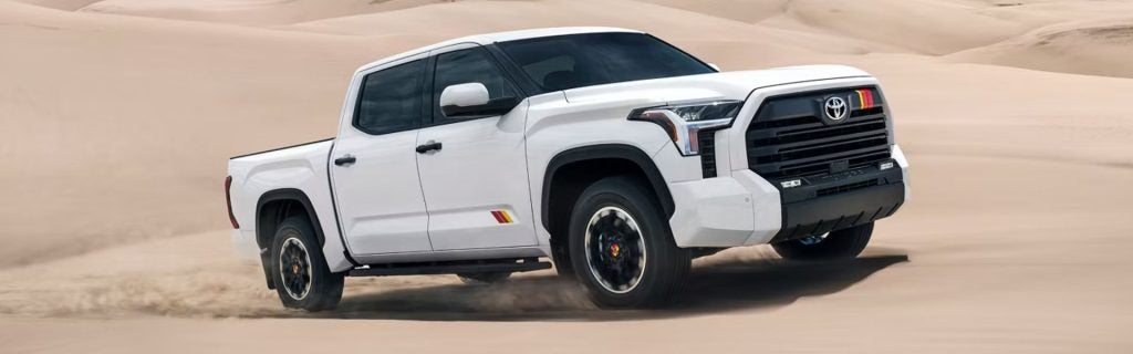 White Toyota Tundra pickup truck kicking up dust while driving through sand dunes