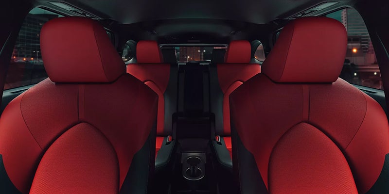 Interior view of a car with rows of deep red seats and a central console with cup holders visible.