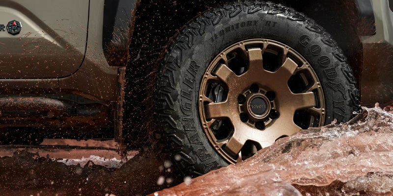 Right front side of a brown Toyota pickup with a brown wheel driving through splashing muddy water.