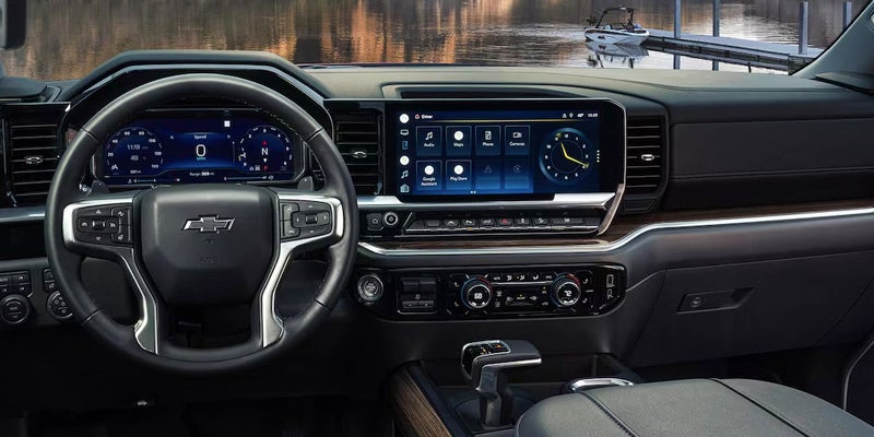 Interior of a modern Chevrolet truck with a digital dashboard and large infotainment screen displaying apps, overlooking a lake with a boat.