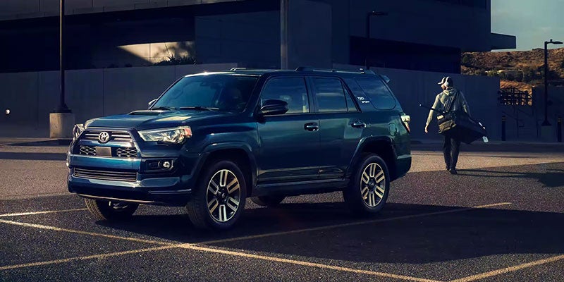 A person with golf clubs walking towards a parked dark blue Toyota 4Runner TRD Sport in a parking lot.