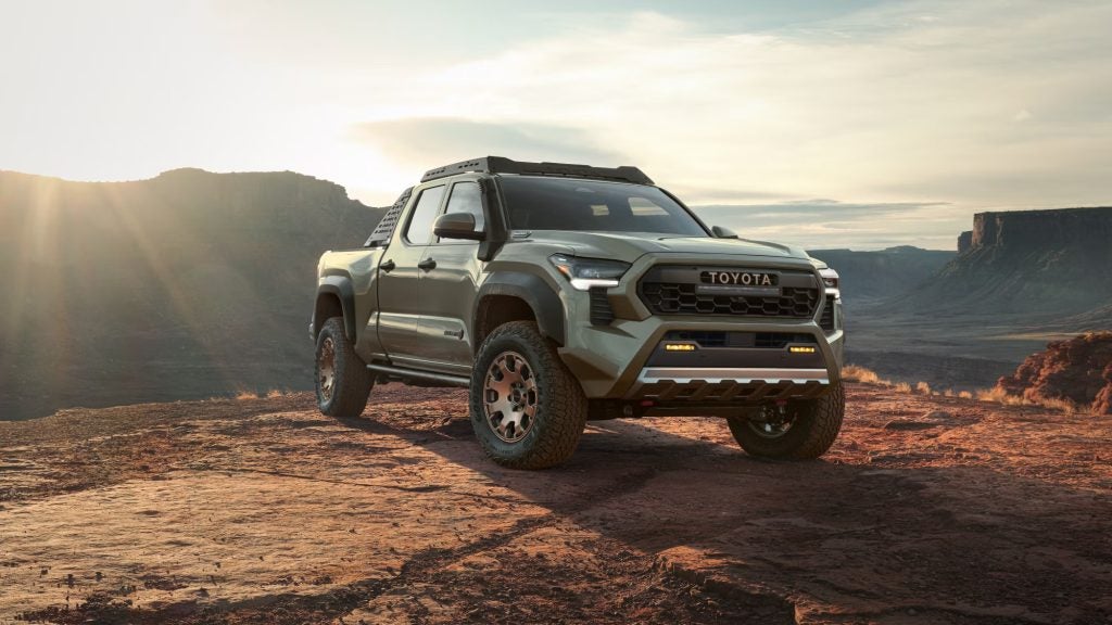 A green Toyota pickup truck with off-road tires, snorkel, and roof rack sits on a rocky cliff overlooking a canyon.