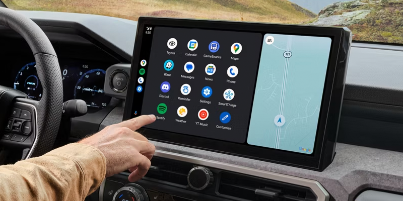 A person's hand touches a car's infotainment screen, displaying app icons and a navigation map.