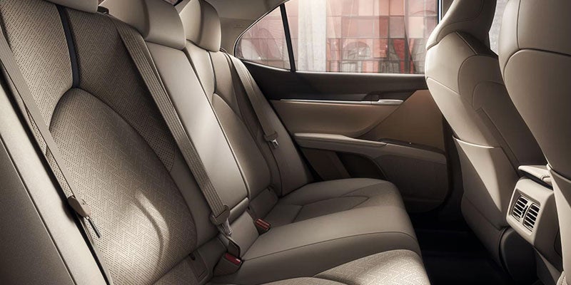 Rear seats of a car with light-colored upholstery, one seatbelt visible.