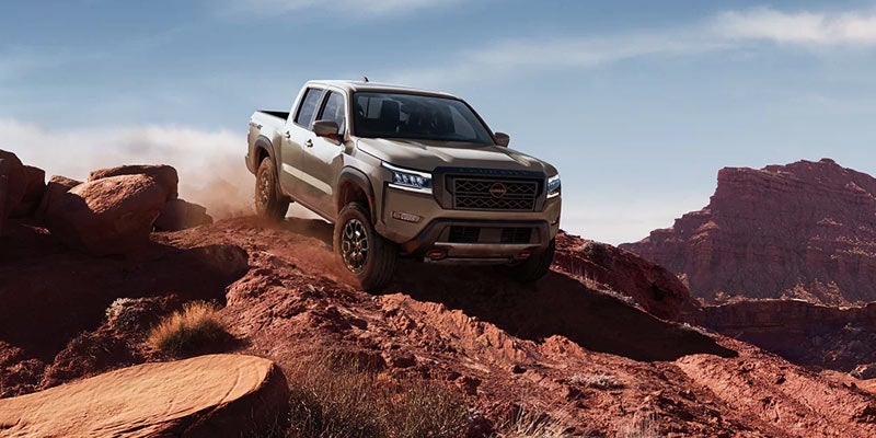 Tan Nissan Frontier PRO-4X pickup truck driving on red rocky desert terrain, kicking up dust