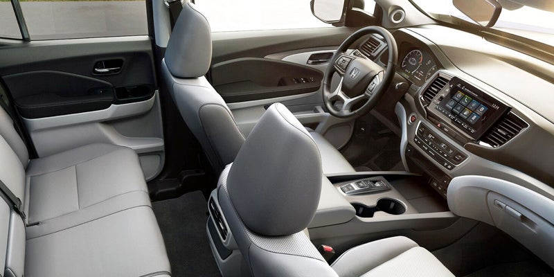 Interior of a car's left side, showing gray leather seats, dashboard, steering wheel, and infotainment screen.