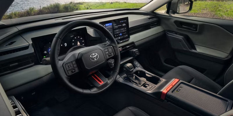 The interior of a Toyota showing the dashboard, steering wheel, digital displays, and center console, with a natural landscape seen through the windshield.