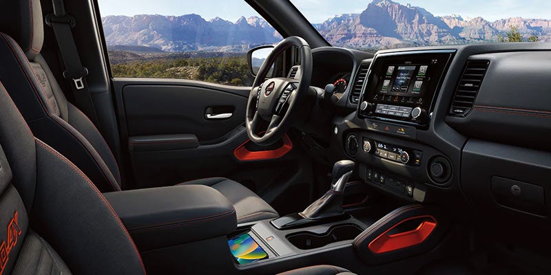 Interior view of a dark grey car, features include vibrant orange accents, a large touchscreen, and a mountain landscape visible through the windshield.