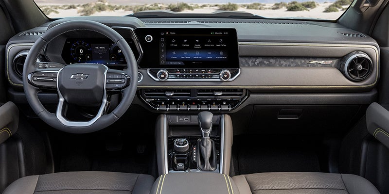 Interior of a Chevrolet pickup truck with a large infotainment screen, digital gauges, yellow accent stitching.