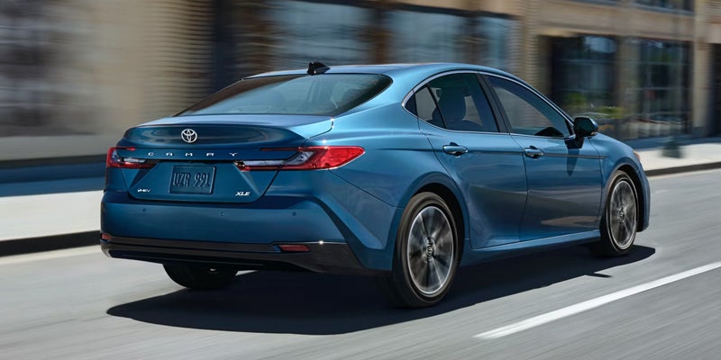 Rear view of a blue Toyota Camry XLE driving on a city street.
