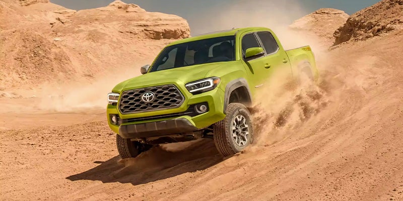 Lime green Toyota Tacoma pickup truck kicking up dust as it drives up an incline in a desert canyon.