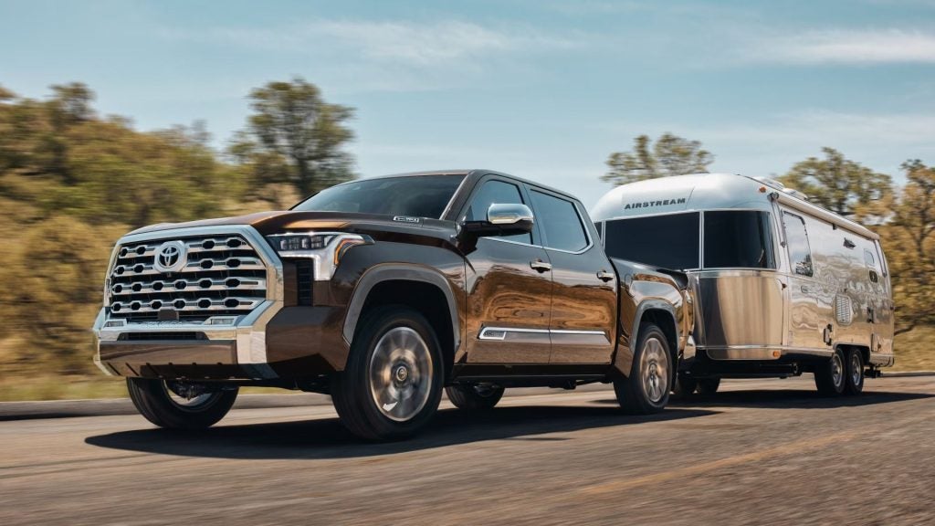 A brown Toyota Tundra pickup truck tows a silver Airstream travel trailer down a highway.