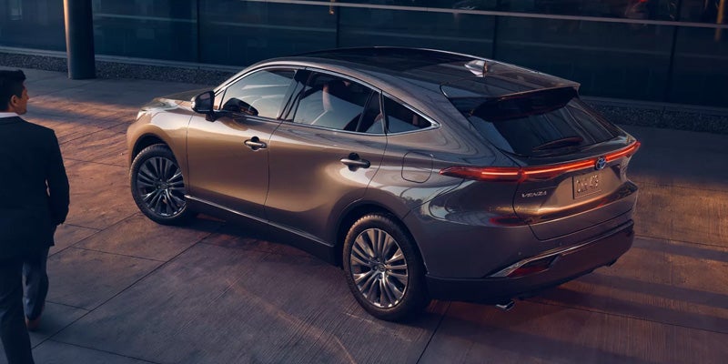 A man in a suit approaches a shiny, bronze-colored Toyota Venza parked on a paved surface.
